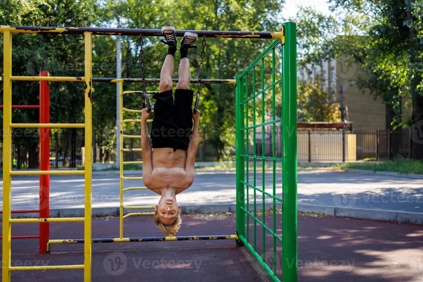 The boy hung upside down on the sports rings with his hands on them. Street workout on a horizontal bar in the school park. photo