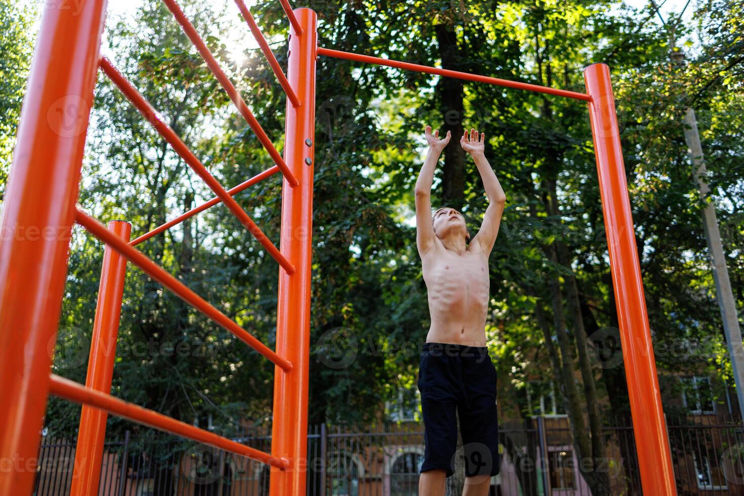An athletic child in the park tries to jump up and grab the bar. Street workout on a horizontal bar in the school park. photo