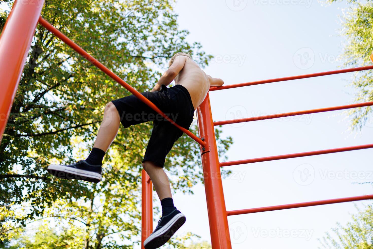 View from the bottom of a teenager who sits on a gymnastic crossbar and watches. Street workout on a horizontal bar in the school park. photo