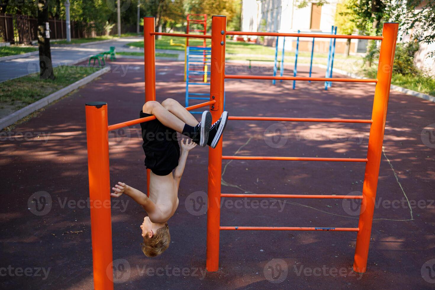 a teenager of an athletic build hangs head down, clinging to the horizontal bar with his feet. Street workout on a horizontal bar in the school park. photo