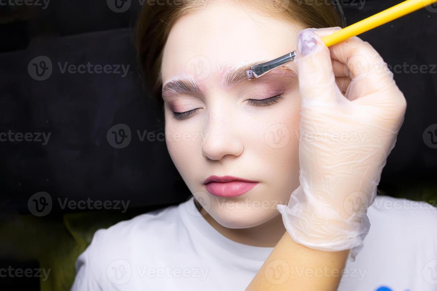 a young blonde model in the eyebrow lamination procedure, the master uses a brush to apply laminating compounds to the eyebrows photo