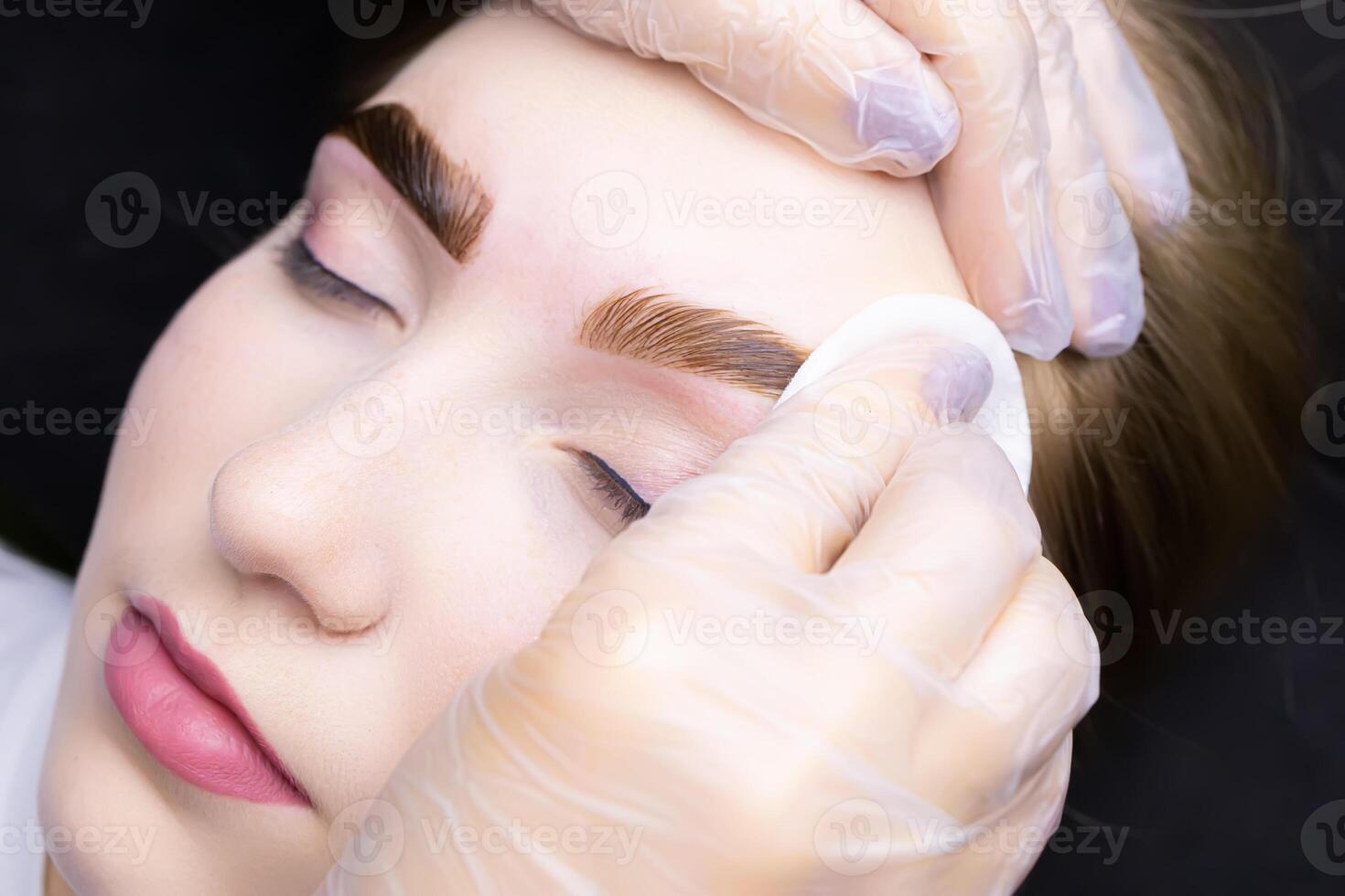 the master removes the remnants of paint from the eyebrows of the model with a cotton sponge photo