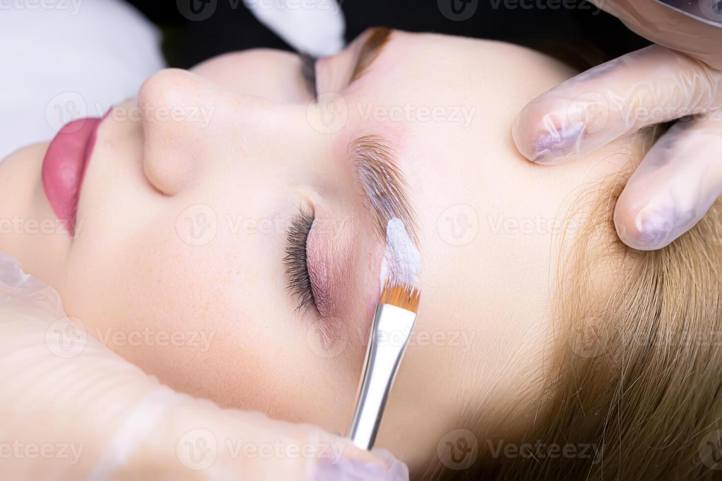 applying laminating compositions to the model's eyebrow in close-up using a brush photo