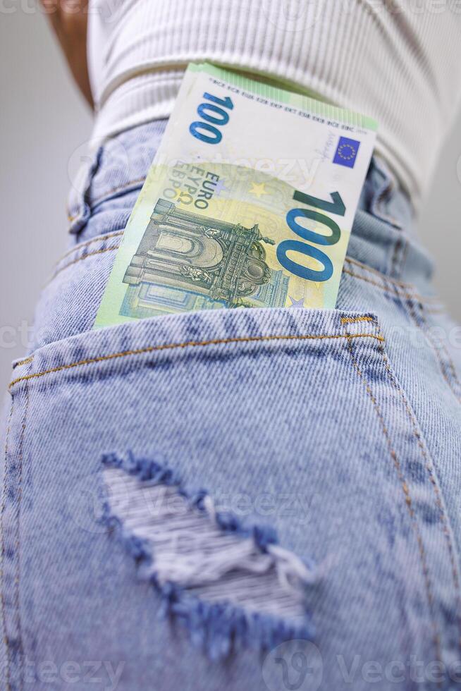 A close-up of a hundred euro bill sticking out of the back pocket of his jeans. A girl in jeans with a euro banknote in her hands. photo