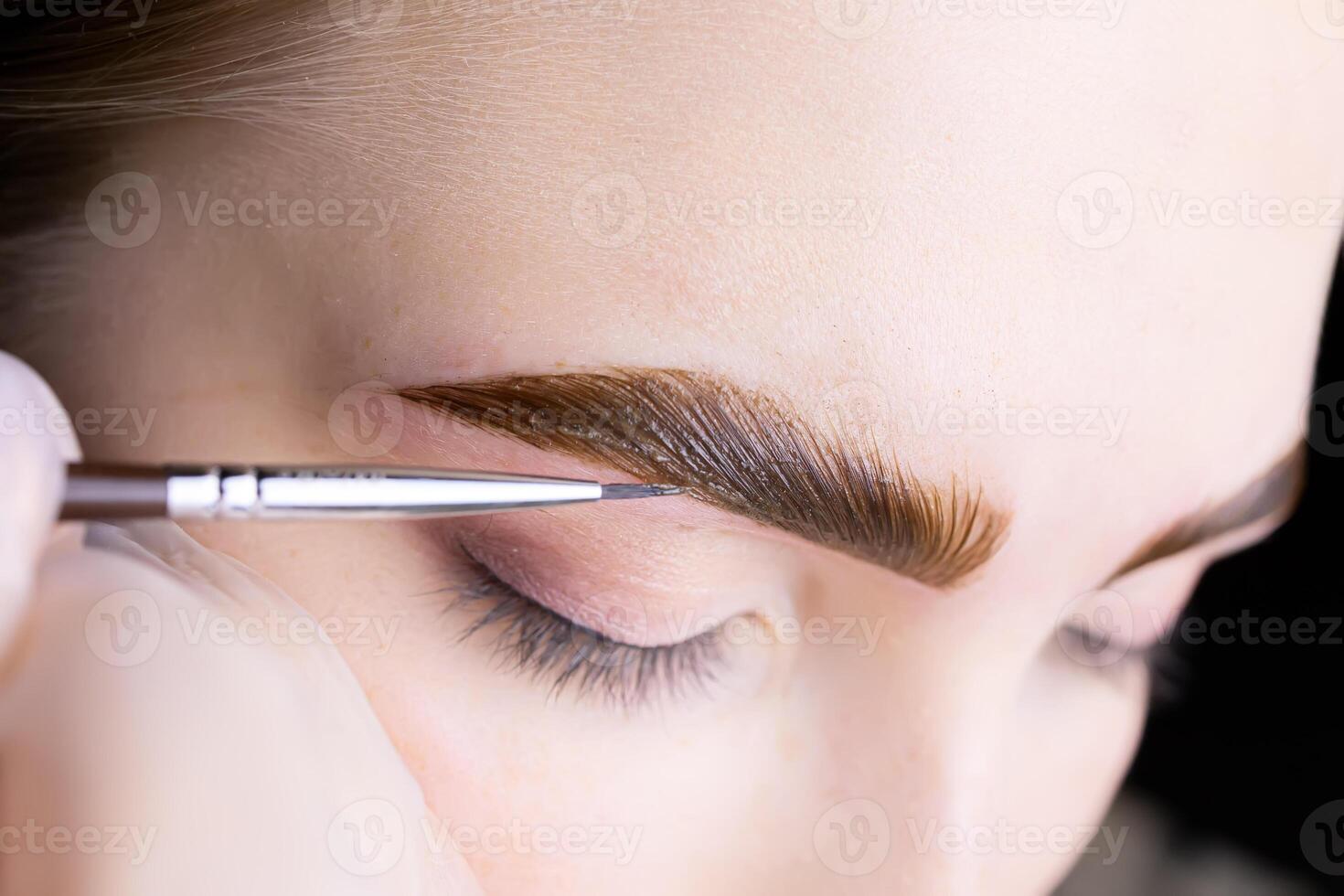 in the hands of the master, a thin brown brush with which he applies eyebrow paint to the hairs after the lamination procedure photo