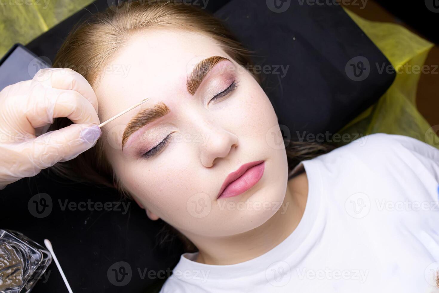 the face of a blonde model who is lying on the couch in a white T-shirt, with paint applied on her eyebrows photo