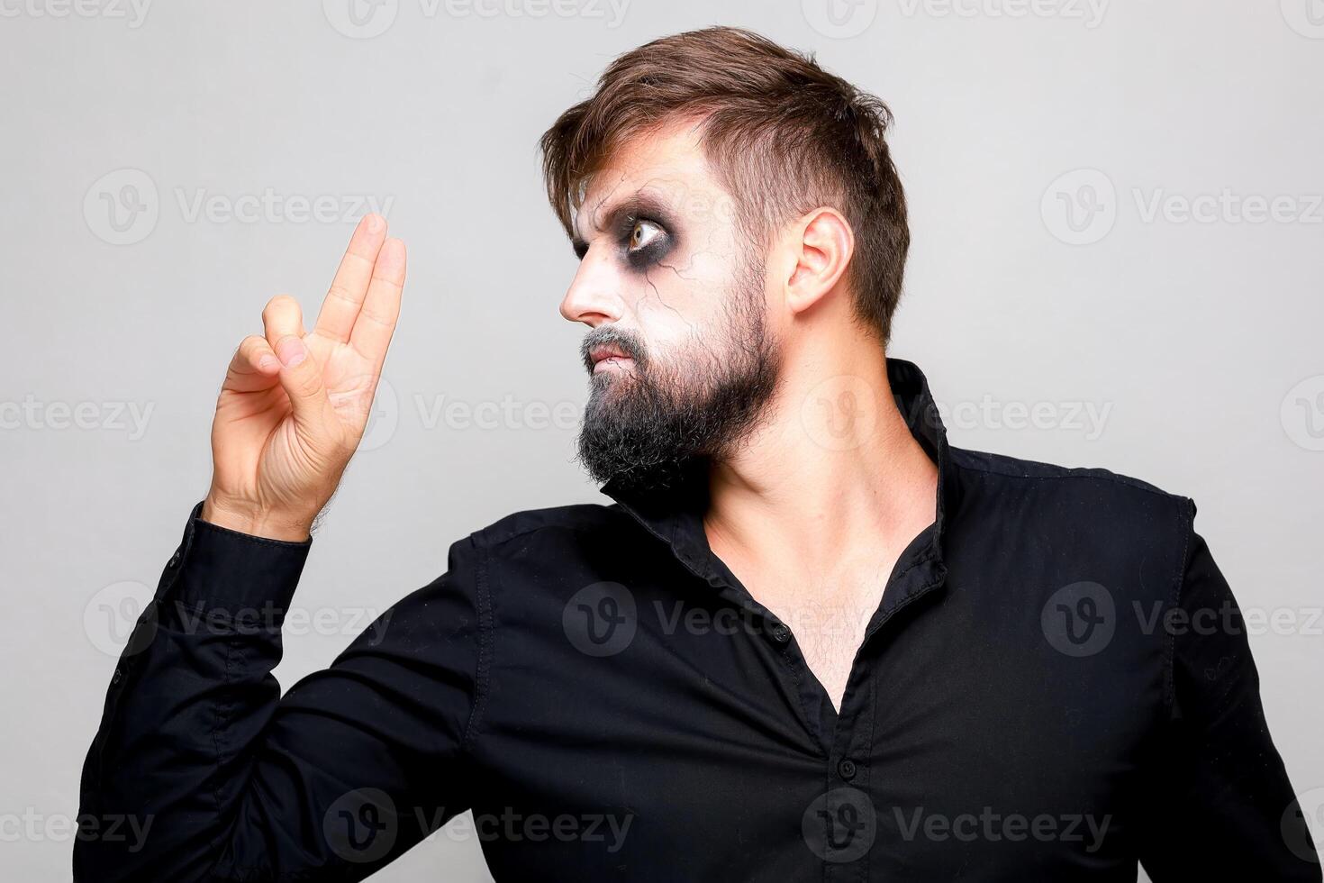 un hombre con muertos vivientes maquillaje para Víspera de Todos los Santos sostiene su manos en frente de él y mira a el cámara desde debajo su frente foto