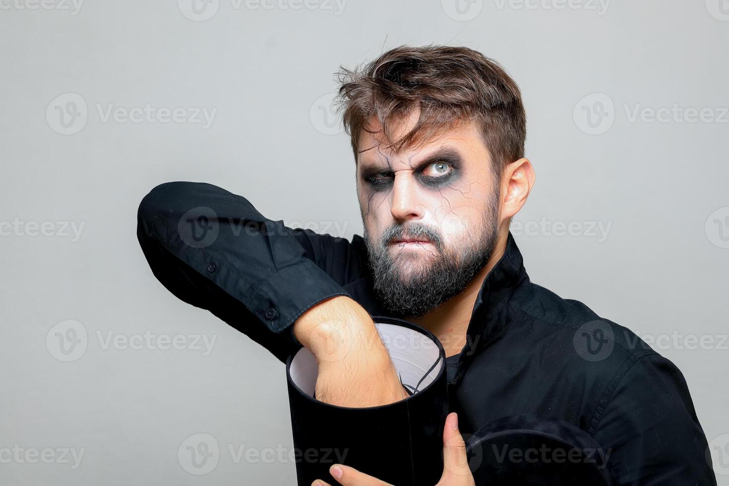 a man with a beard and makeup for Halloween holds a black box with gifts in his hands photo