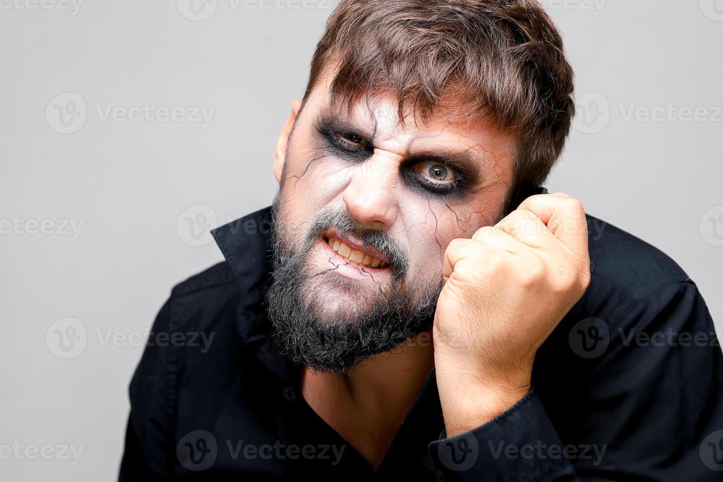 portrait of a bearded man with undead-style makeup who holds his hand near his head photo