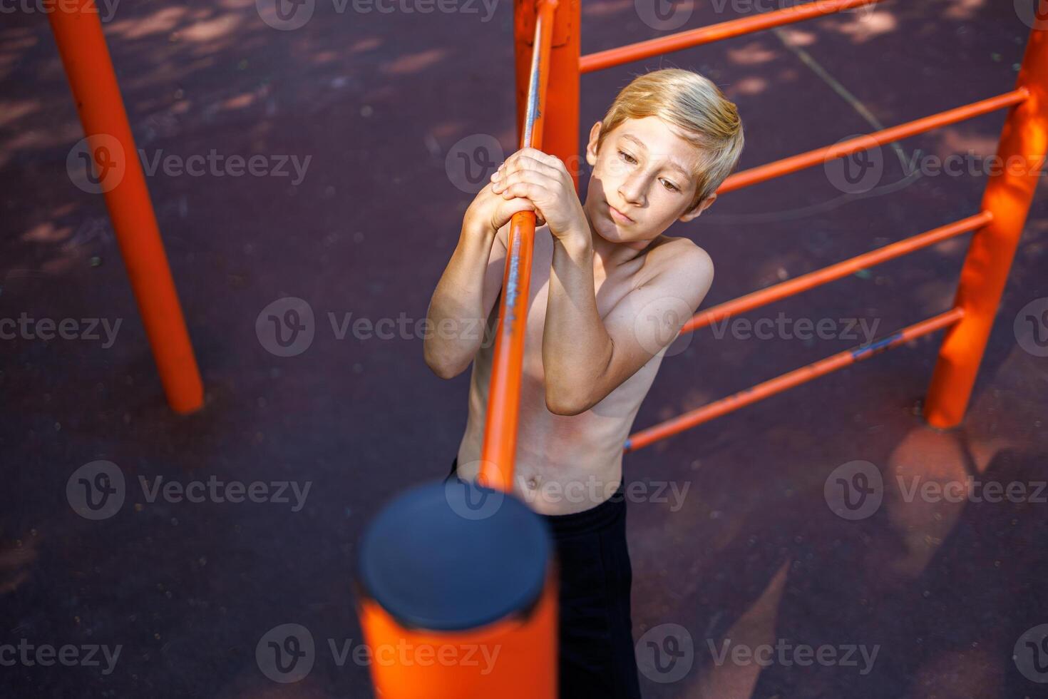 Sports child performs a side pull-up on the crossbar. Street workout on a horizontal bar in the school park. photo