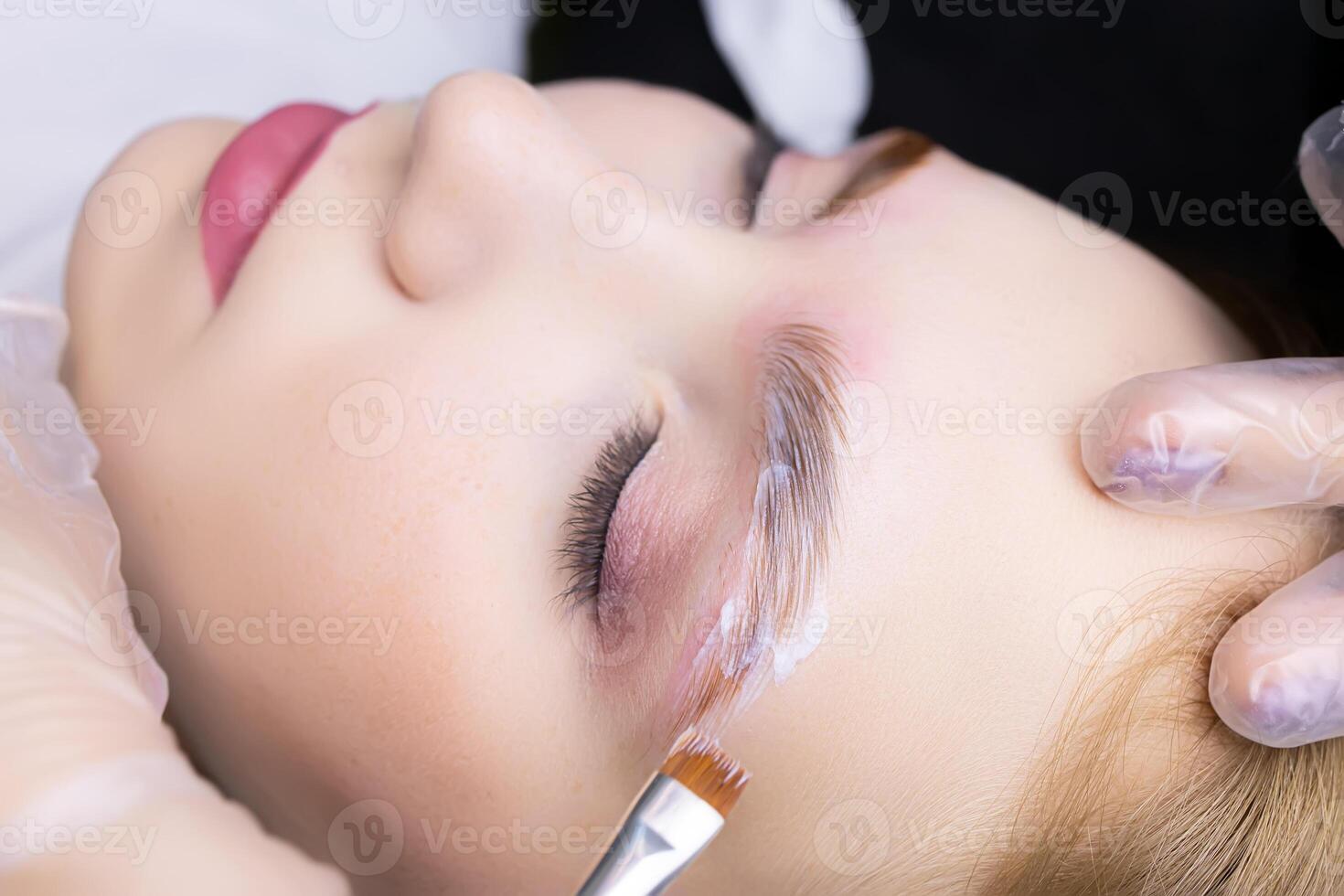applying laminating compositions to the model's eyebrow in close-up using a brush photo