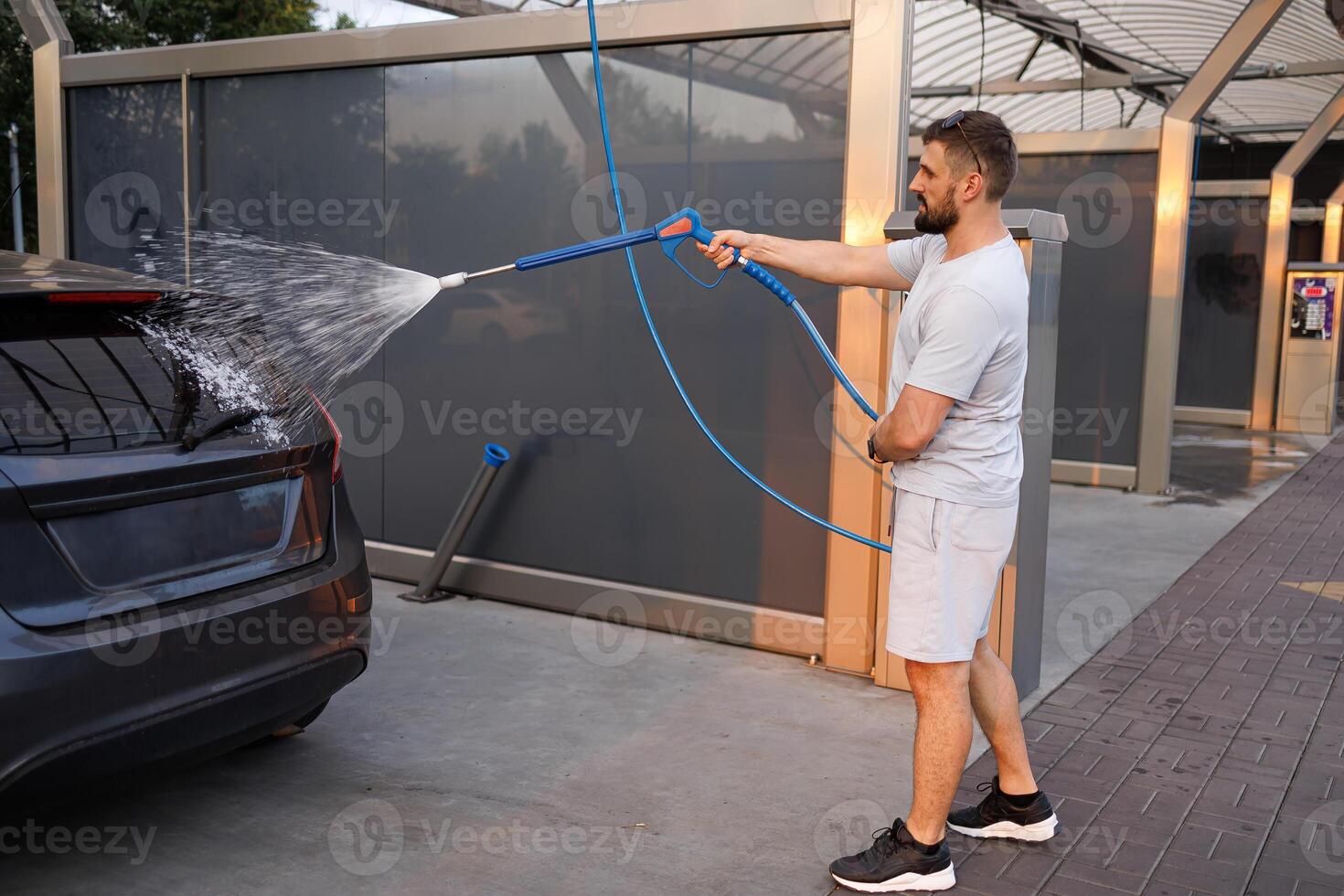 A man points a foam sprayer at a car. A car at a self service car wash. photo