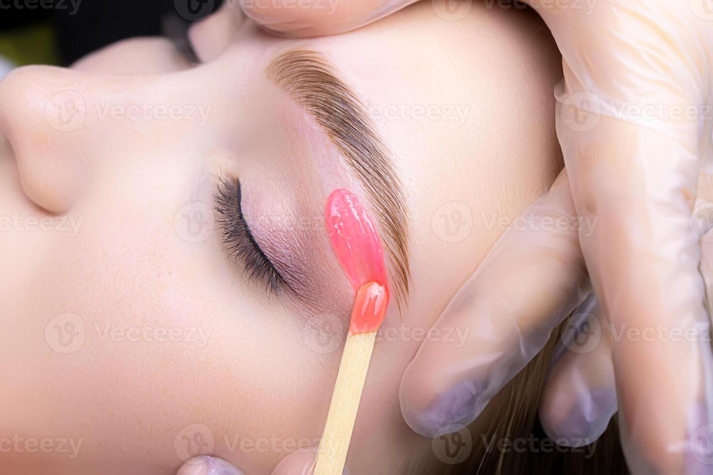 close-up of applying red wax to remove unwanted hairs from the lower contour of the model's eyebrows photo