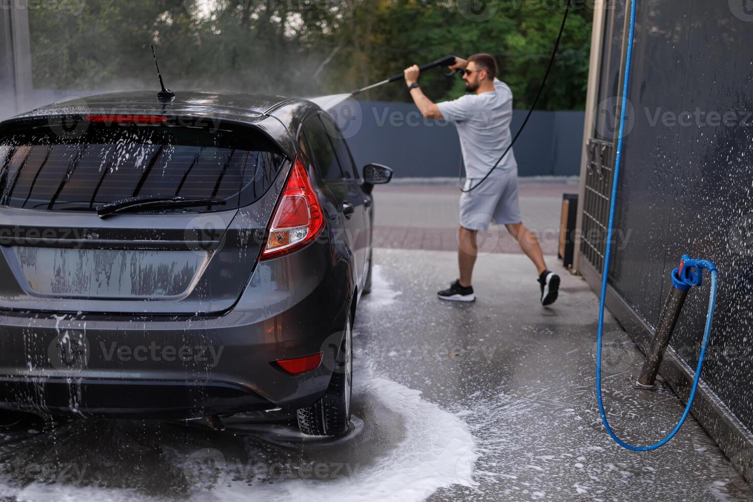 The car at the car wash, which in the background is washed with a water cannon by a man. A car at a self service car wash. photo