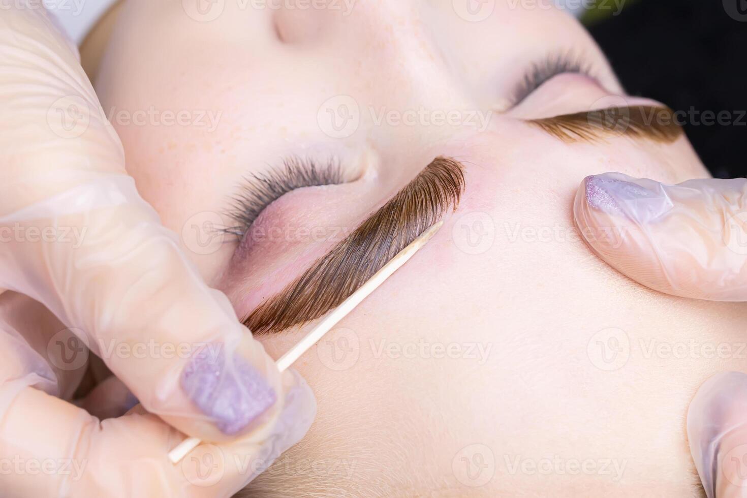 macro photography of the model's eyebrows painted and applied eyebrow paint on them, the master tries to remove excess paint from the contour of the eyebrows with a cotton swab photo