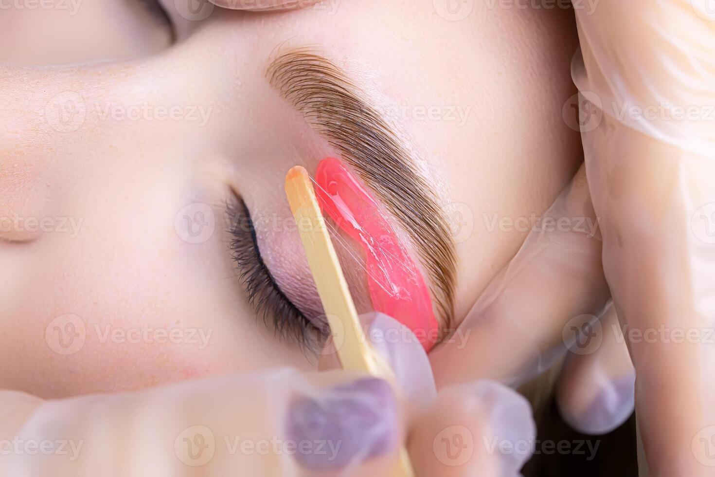 the hands of the master white gloves stretch the eyebrow of the model apply wax to remove unwanted hairs after the procedure of coloring and lamination photo