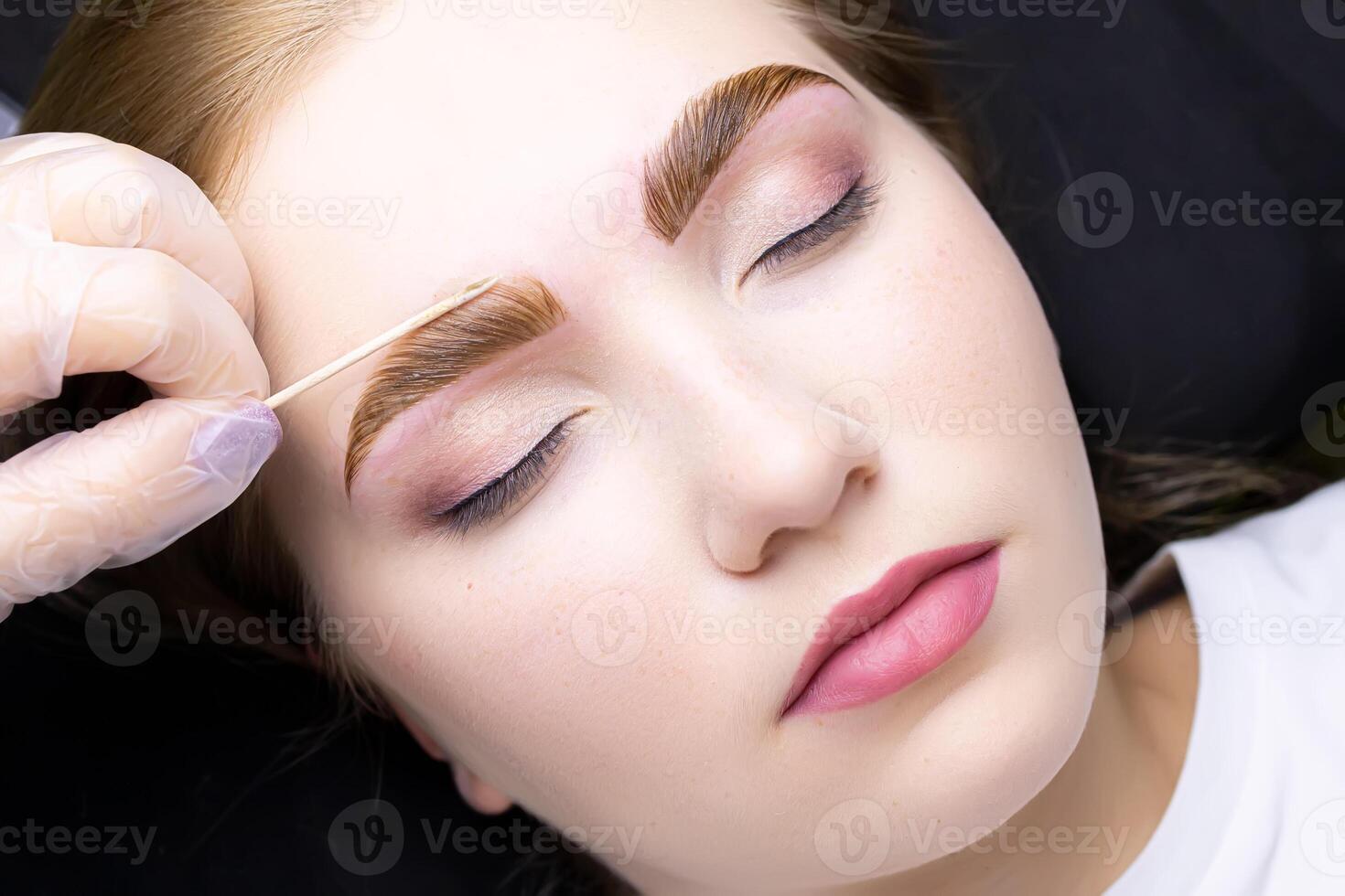 the face of a blonde model who is lying on the couch in a white T-shirt, with paint applied on her eyebrows photo