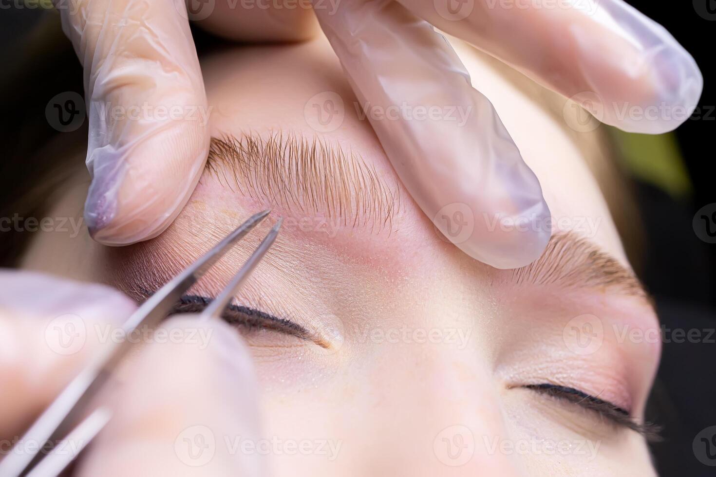 macro photography of the laid eyebrows with the help of lamination, the master tweezers pluck the contour of the eyebrows from excess hairs photo