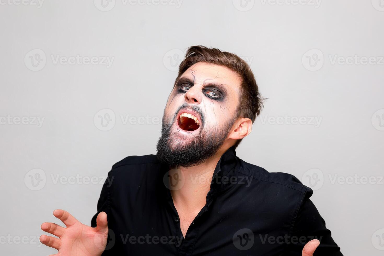 un hombre con un barba y maquillaje en el estilo de el muertos vivientes en Víspera de Todos los Santos abrió su boca y muestra su dientes foto