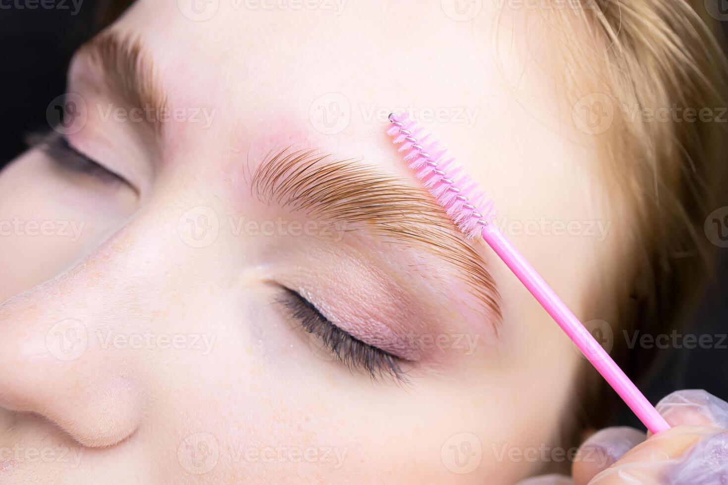 a close-up of the eyebrows on which lamination is performed and the master combs with a brush directing the growth of eyebrow hair photo