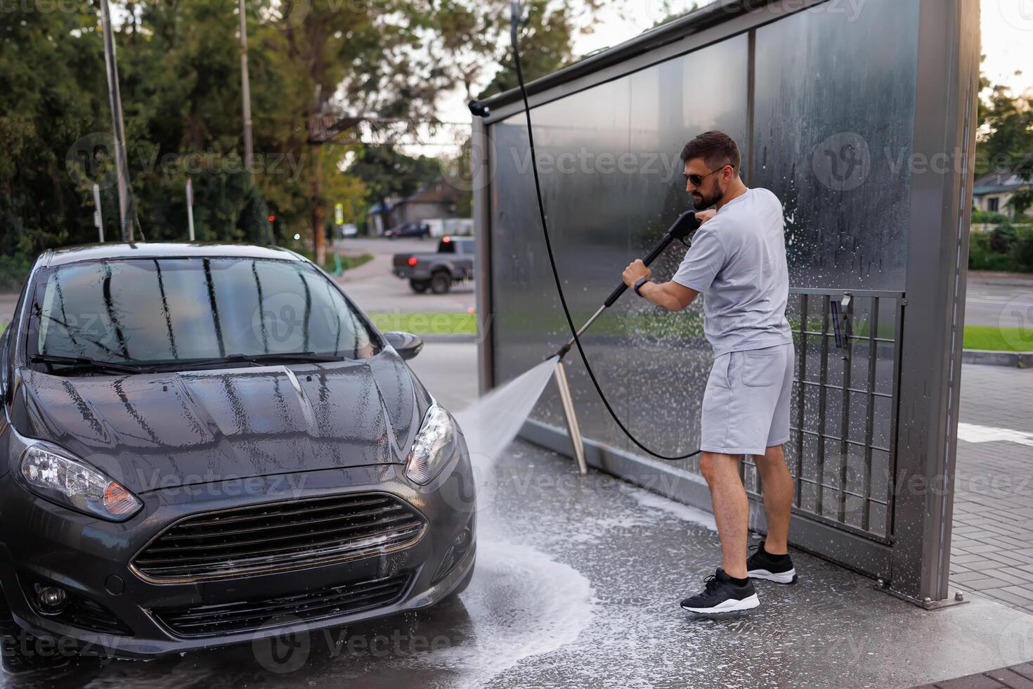 The front part of the car being washed by a man using a water cannon. A car at a self service car wash. photo