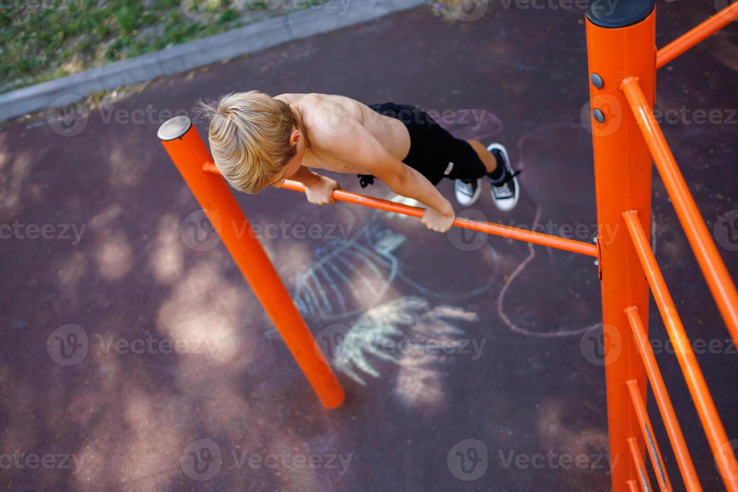 Sports teenager on the horizontal bar performs acrobatic exercises. Street workout on a horizontal bar in the school park. photo