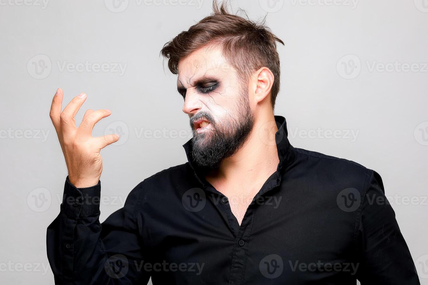 Scary undead-style makeup for Halloween on a bearded man who shows gestures photo