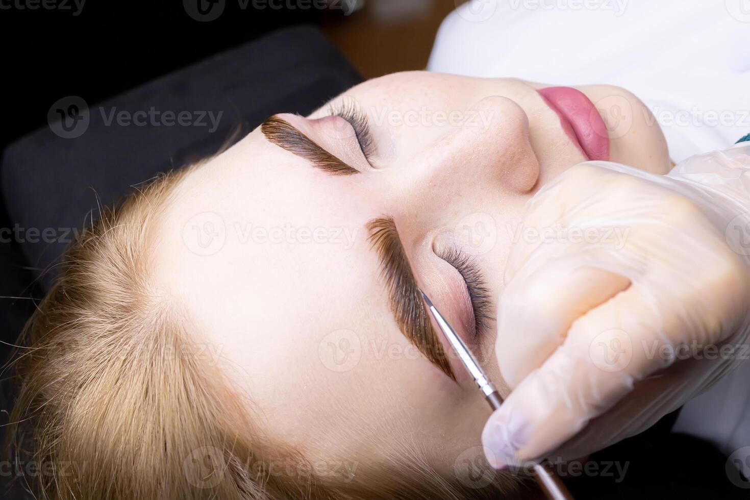 in the hands of the master, a thin brown brush with which he applies eyebrow paint to the hairs after the lamination procedure photo