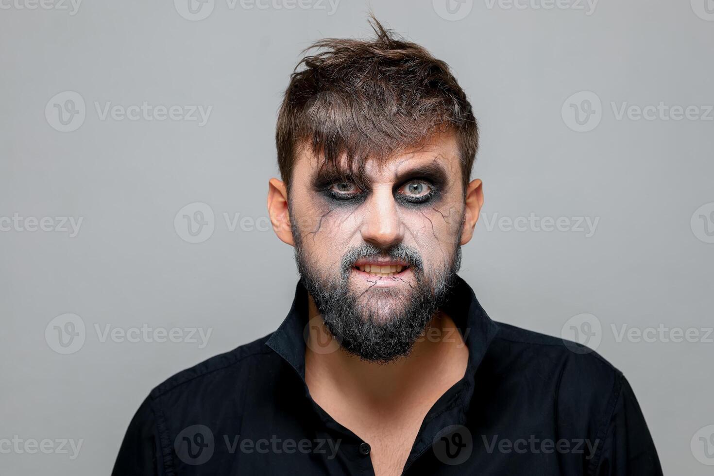 un hombre en un negro camisa soportes en un blanco antecedentes quien tiene estilo no-muerto maquillaje para Víspera de Todos los Santos foto