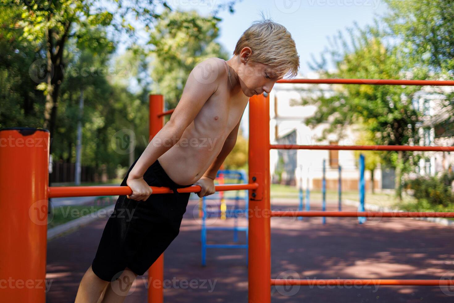 Athletic boy stretched upward and holding onto the tourniquet with his hands. Street workout on a horizontal bar in the school park. photo