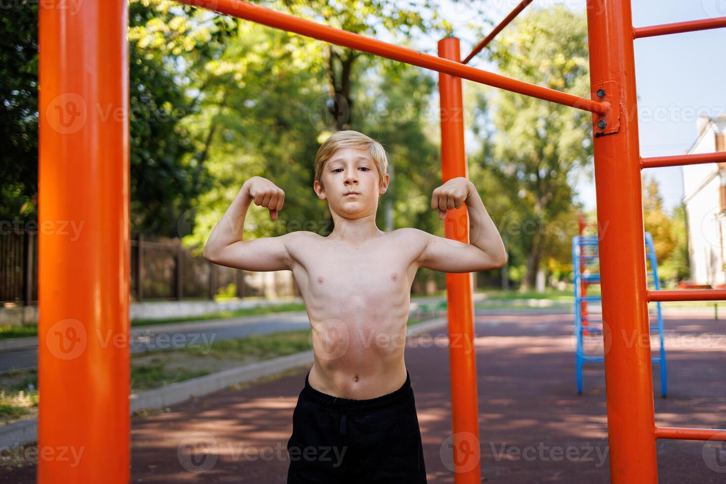 A teenage boy with an athletic build shows off his musculature. Street workout on a horizontal bar in the school park. photo