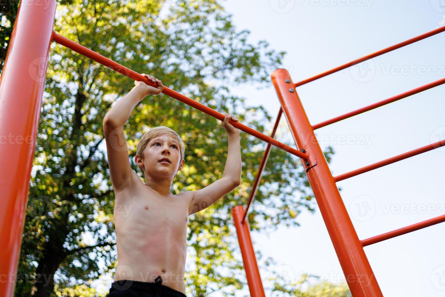 Bottom view of a gymnast boy holding on to a sports bar. Street workout on a horizontal bar in the school park. photo
