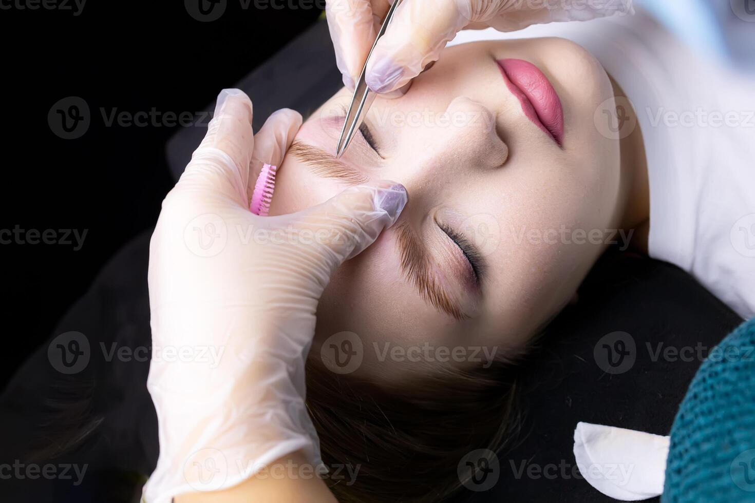 the hands of the master in white gloves stretch the eyebrow and pluck out excess hairs along the contour of the eyebrows photo