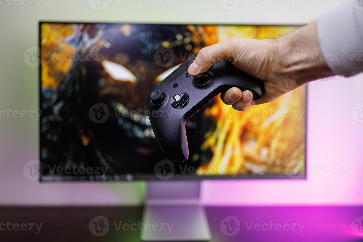 A man's hand holding a gamepad in front of the monitor. game gamepad in hand photo
