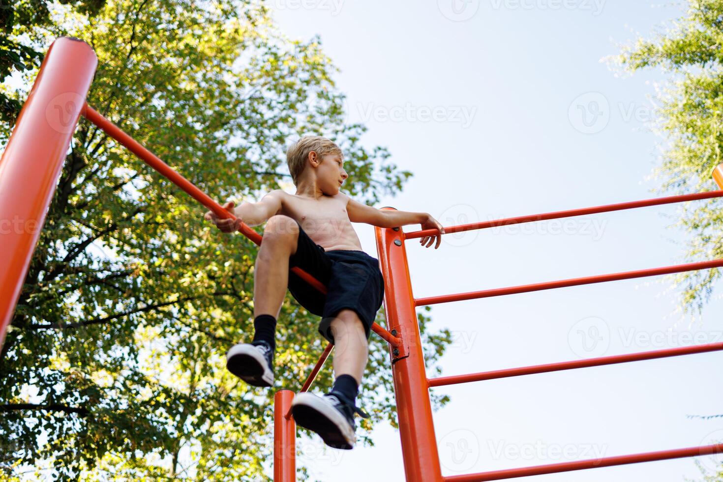 A teenager who climbed into a gym sits there and rests. Street workout on a horizontal bar in the school park. photo