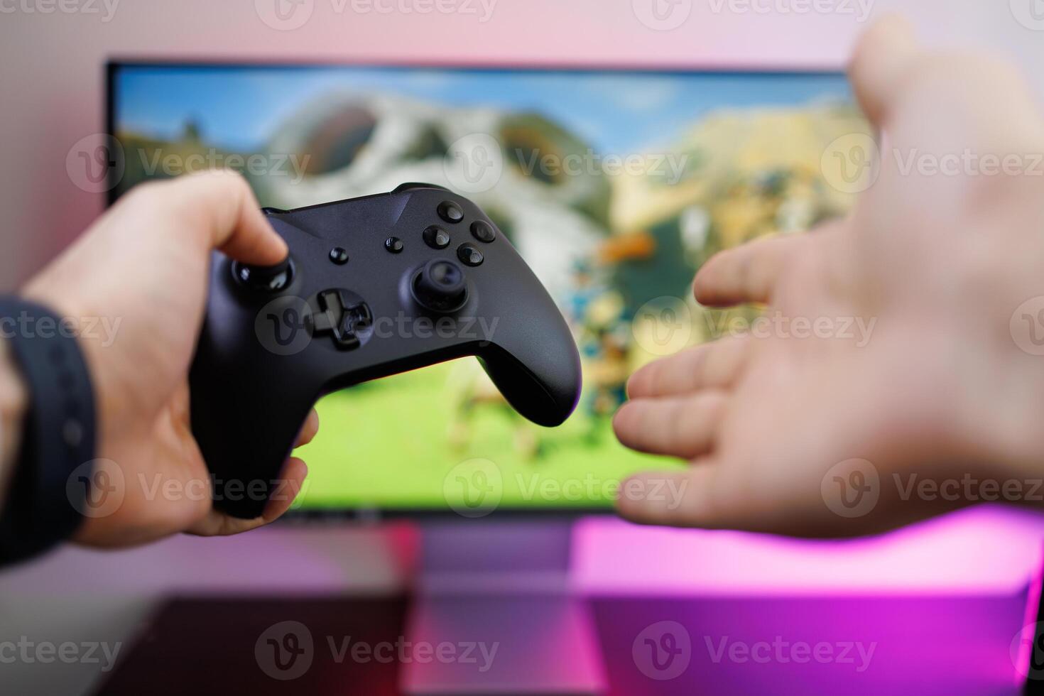 Holding a game gamepad in one hand and using the other hand to point at the monitor that's in the background. game gamepad in hand photo