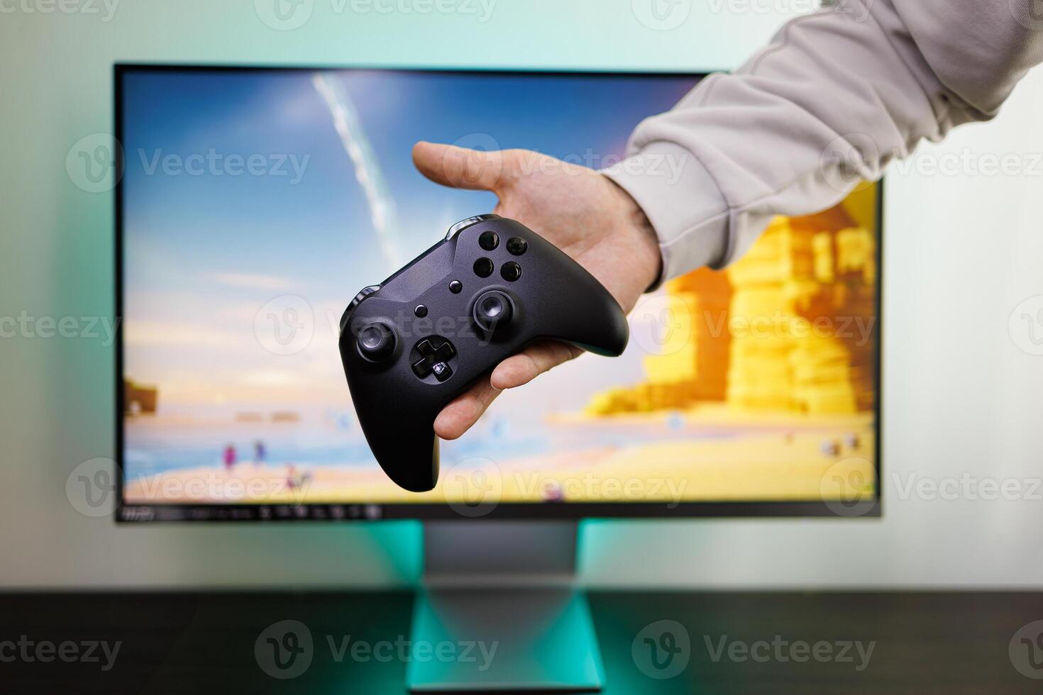 en el antecedentes de un juego monitor, un del hombre mano sostiene un controlador en el palma de su mano. juego gamepad en mano foto