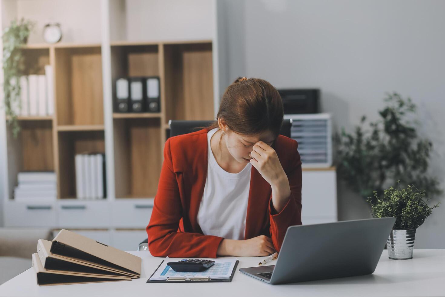 Asian women sitting in a home office With stress and eye strain.Tired businesswoman holding eyeglasses and massaging nose bridge. There are tablets, laptops, and coffee. photo