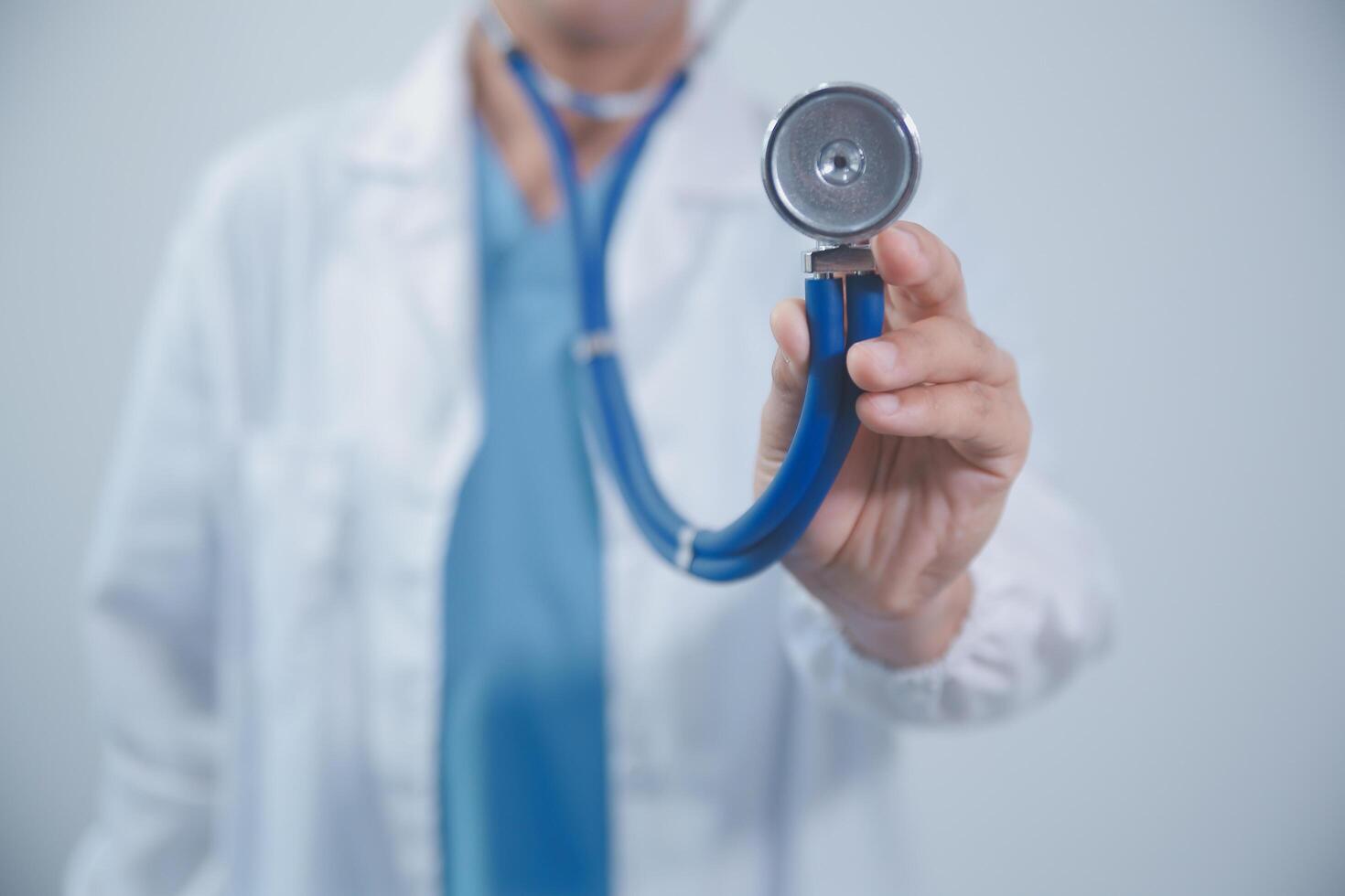 Senior doctor wearing white coat standing holding stethoscope in hands. Older male physician healthcare professional showing medical equipment ready to listen lungs or heart concept. Close up view photo