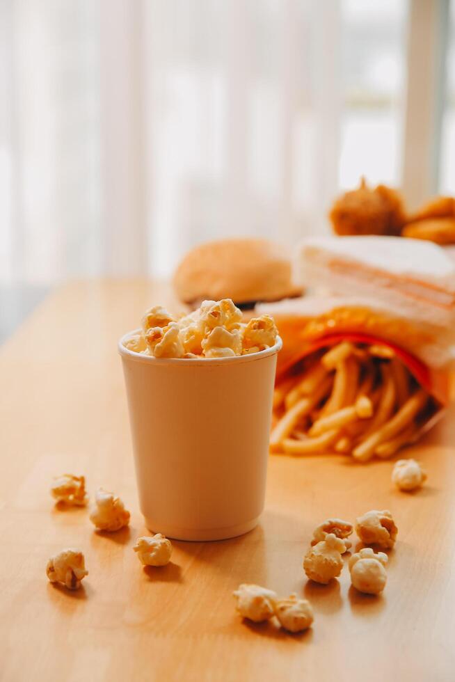 A bucket of popcorn, top-view, warm colors, light brown wooden background, flat lay, daylight macro close-up photo