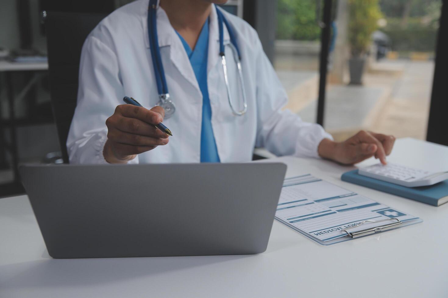 A professional and focused Asian female doctor in scrubs is working and reading medical research on her laptop in her office at a hospital. photo