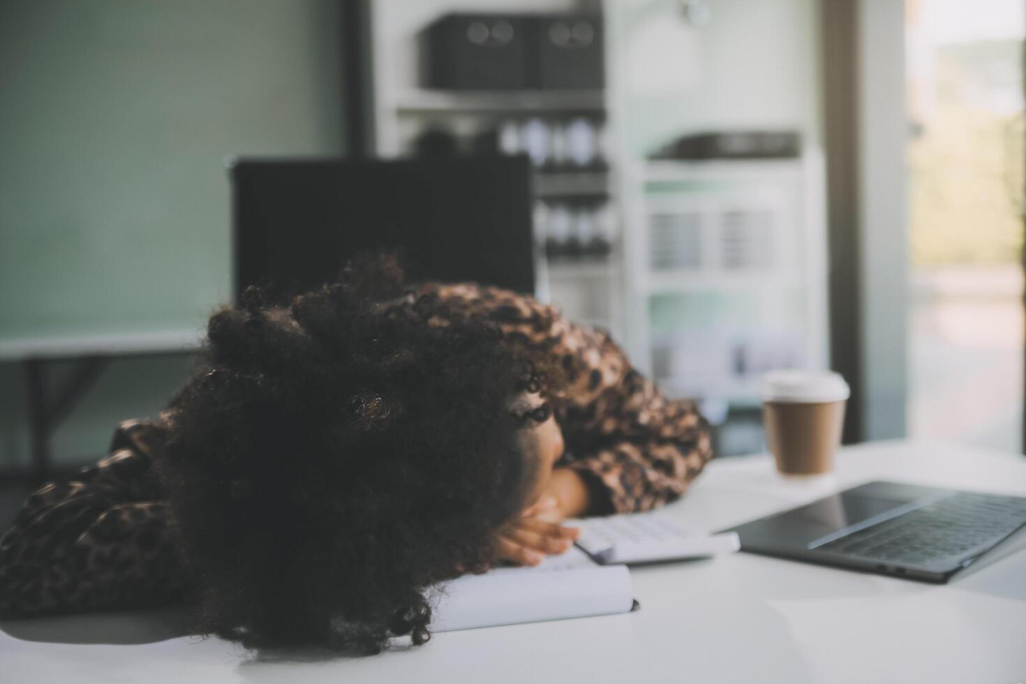 Young woman her head at office desk in front of laptop, feeling ruined, suffer from anxiety, about to attempt suicide, pregnancy, end of a working day, exhausted and unable to manage her emotions photo