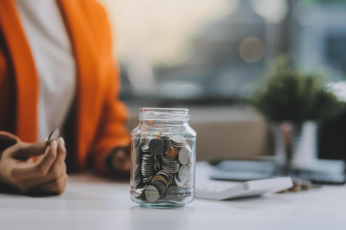 Beautiful Asian businesswoman insert coins in a pin piggy bank on the table. saving money, investment, currency concept photo
