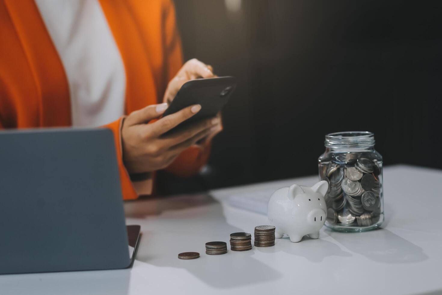 Beautiful Asian businesswoman insert coins in a pin piggy bank on the table. saving money, investment, currency concept photo