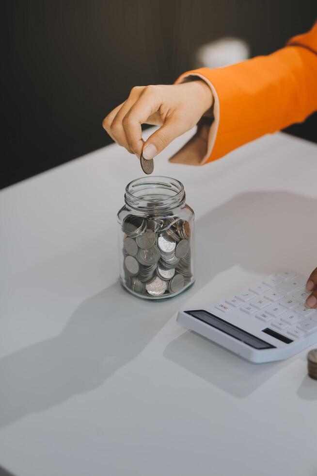 Beautiful Asian businesswoman insert coins in a pin piggy bank on the table. saving money, investment, currency concept photo