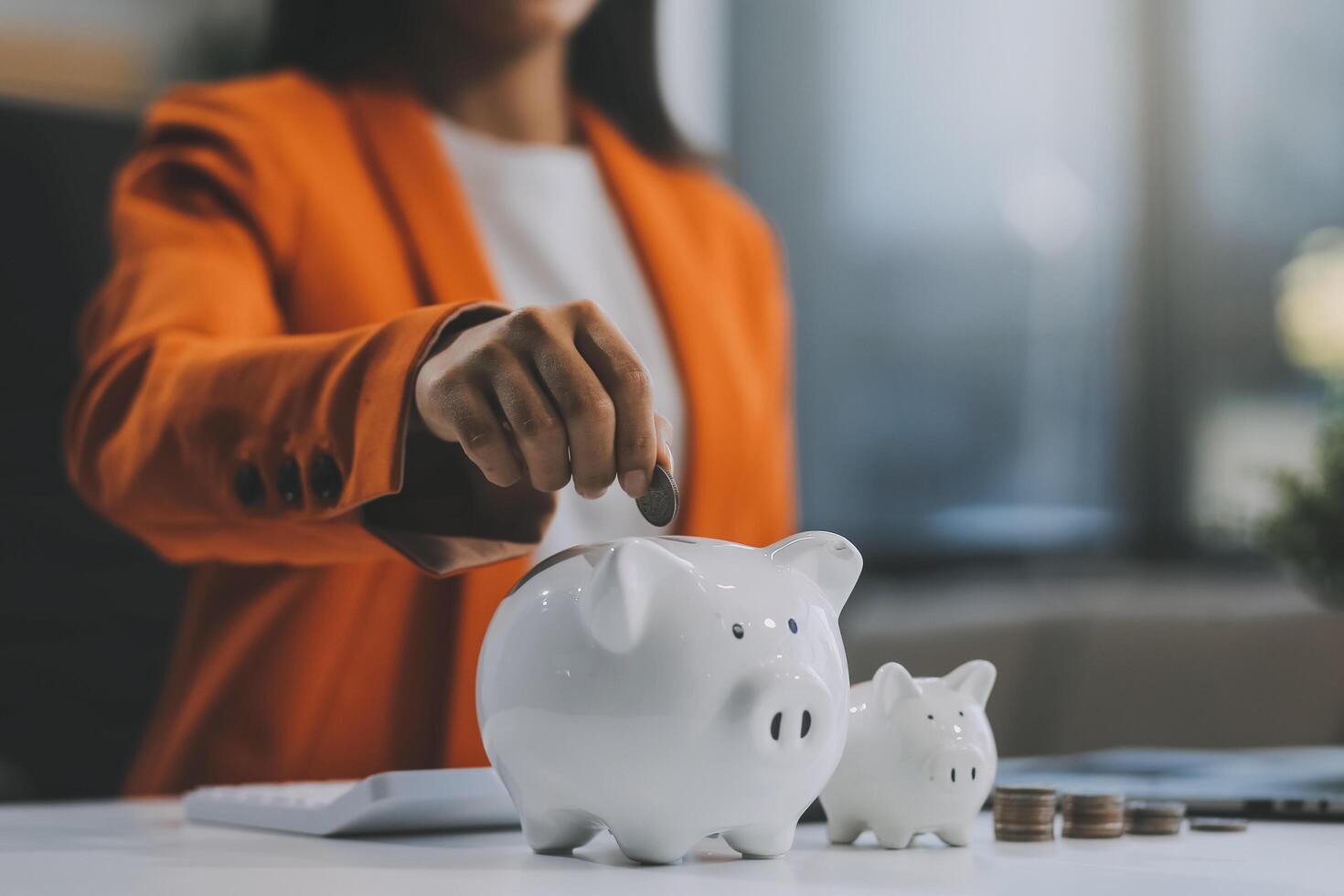 Beautiful Asian businesswoman insert coins in a pin piggy bank on the table. saving money, investment, currency concept photo