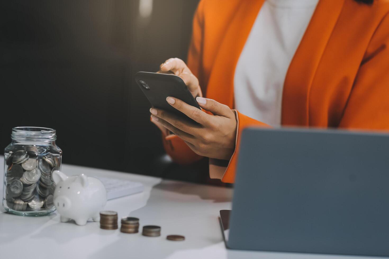 Beautiful Asian businesswoman insert coins in a pin piggy bank on the table. saving money, investment, currency concept photo