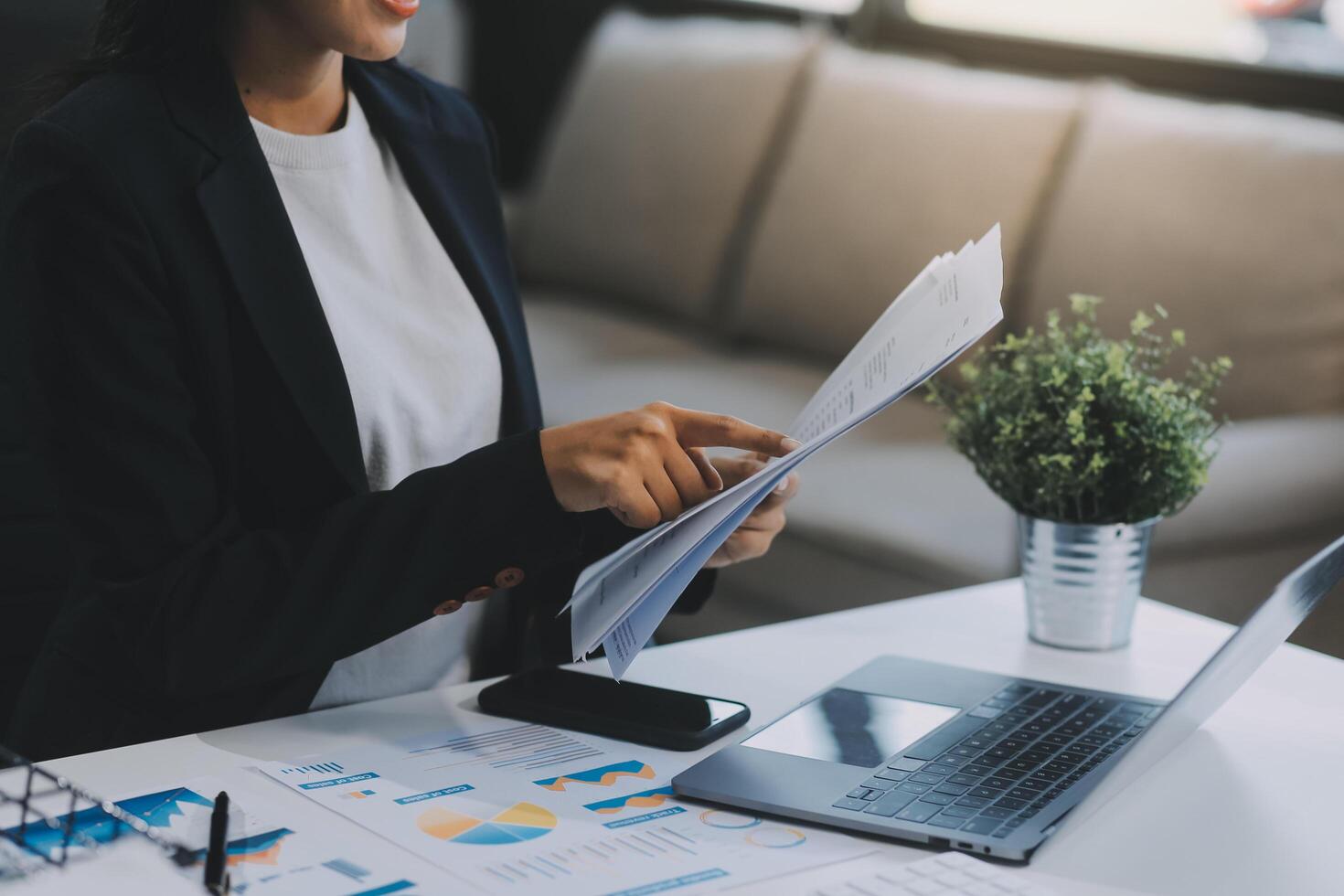 Confident millennial indian female business analyst financial advisor preparing statistic report studying documents on work desk, browsing information online using pc, writing out notes on paper sheet photo