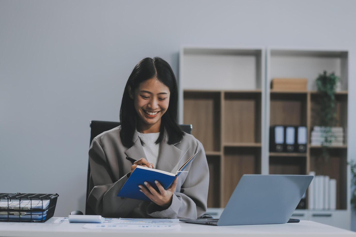 Confident millennial indian female business analyst financial advisor preparing statistic report studying documents on work desk, browsing information online using pc, writing out notes on paper sheet photo