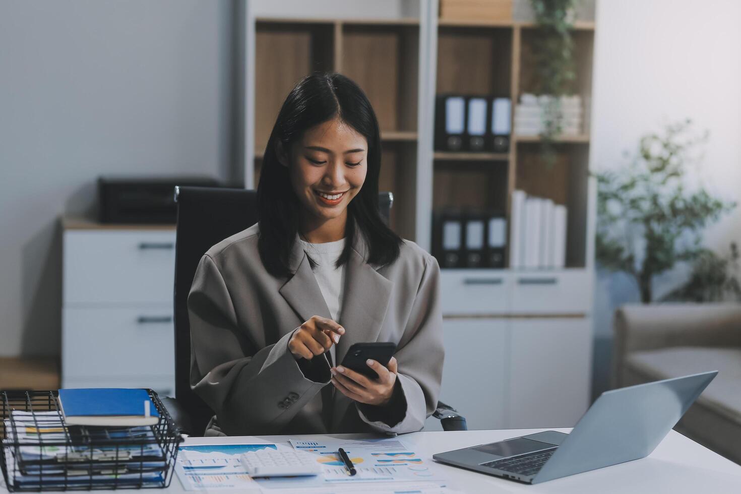 felicidad empresaria hermosa mujer joven asiática de negocios usa un teléfono móvil de uso informal para comprar en línea disfrutar con las redes sociales y una computadora portátil en casa. inicio de una pequeña empresa. banca en línea foto